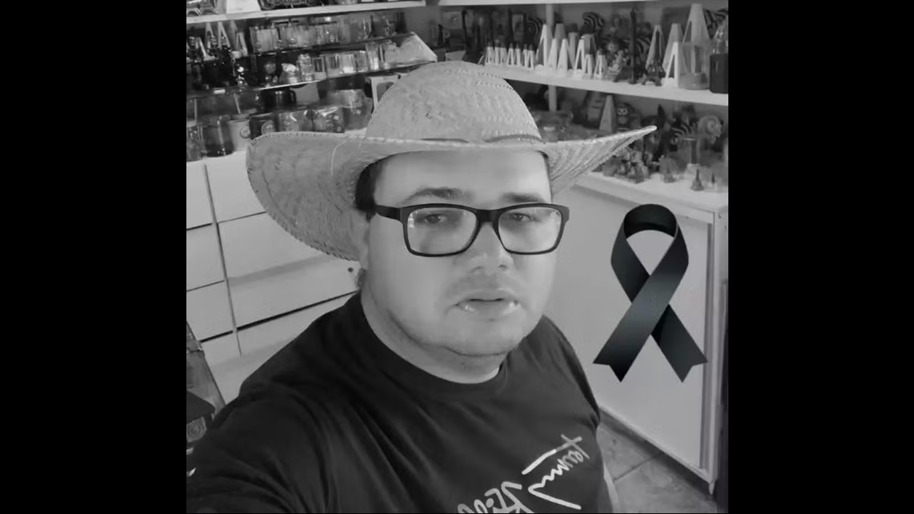 Foto em preto e branco do empresário morto. Ele usa um chapéu grande. Ao lado dele, um laço preto simbolizando luto.