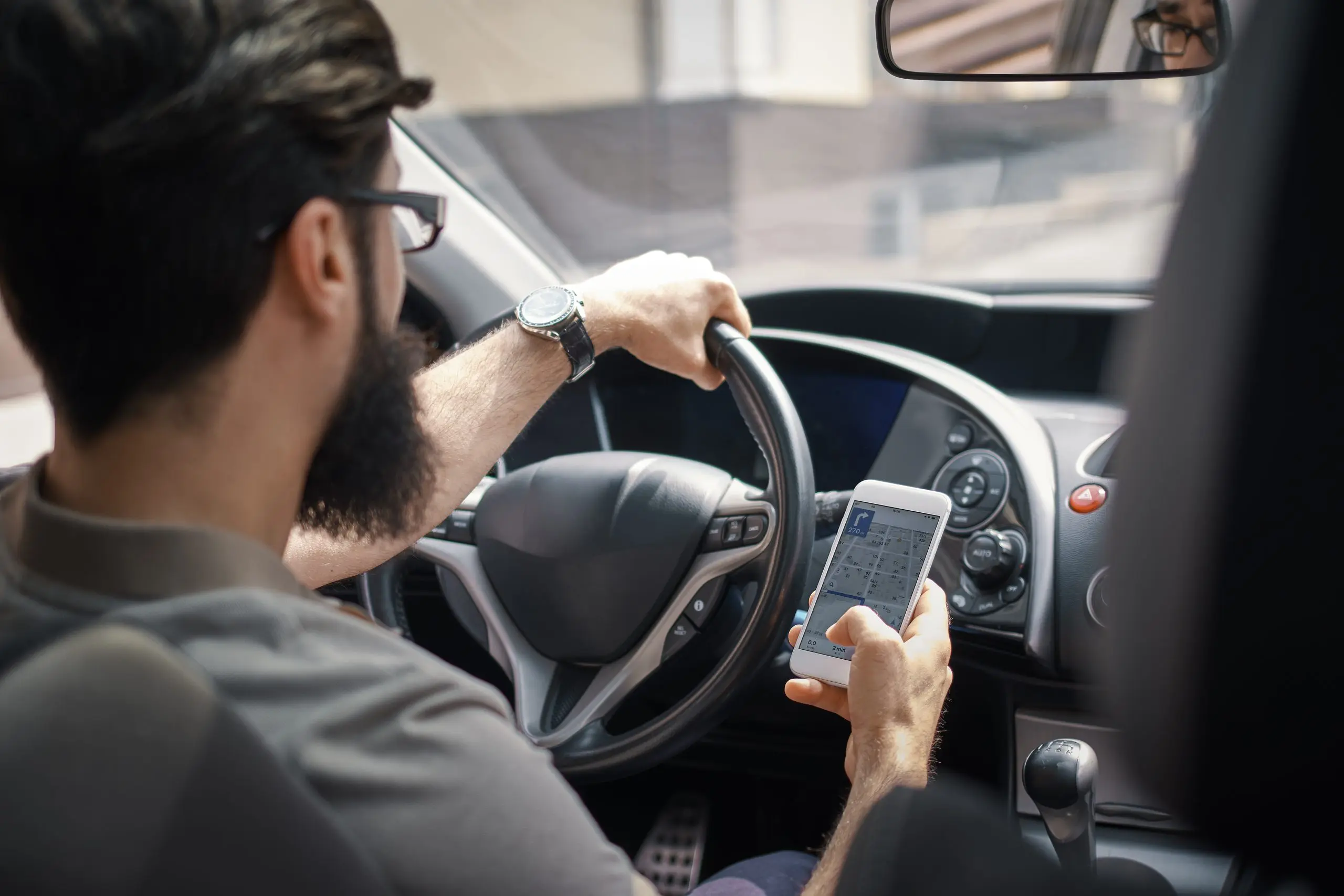 Man searching destination direction or address on gps or navigator application via mobile smartphone inside a car while driving car - back view. Technology, distraction and driving concept