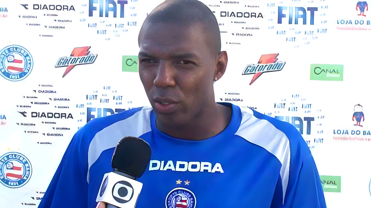 Jogador usa uniforme azul com detalhes brancos. Ele fala ao microfone da TV Bahia.